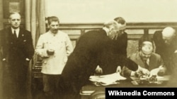 Viaceslav Molotov semnează Tratatul de prietenie dintre URSS și Germania în prezența lui Stalin și a lui Joachim Ribbentrop. Moscova, Kremlin, 23 august 1939.