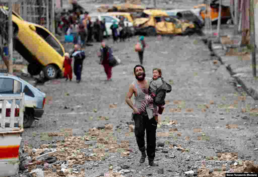 A crying man carries his daughter across enemy lines in the Iraqi city of Mosul from territory controlled by Islamic State militants to positions held by Iraqi special forces, March 4, 2017. (Reuters/Goran Tomasevic)