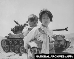Războiul din Coreea a fost descris drept primul război fierbinte din perioada Războiului Rece. Această fotografie arată o tânără, împreună cu fratele ei mai mic, în fața unui tanc M-26. Coreea de Nord a invadat Coreea de Sud în 1950, declanșând acest război.