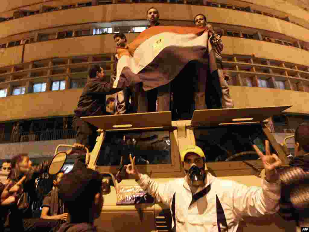 محتجون يحملون علماً مرفرفاً فوق عربة مدرعة خارج مبنى التلفزيون المصري في القاهرة.