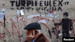 A man walks past a wall in Pristina with graffiti that reads, "The shame of EULEX."