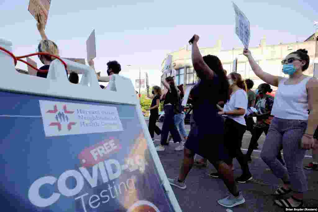 Marchers walk past a sign advertising testing for the coronavirus disease (COVID-19) during a Juneteenth Awareness Walk to demonstrate against racial inequality in the aftermath of the death in Minneapolis police custody of George Floyd, in Boston, Massachusetts, U.S., June 18, 2020. 