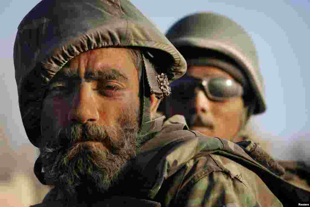 A dust-covered Afghan National Army soldier with a flower tucked behind his ear rides on the back of a vehicle during a patrol near the Taliban stronghold of Panjwaii town, in Kandahar Province, in 2007.