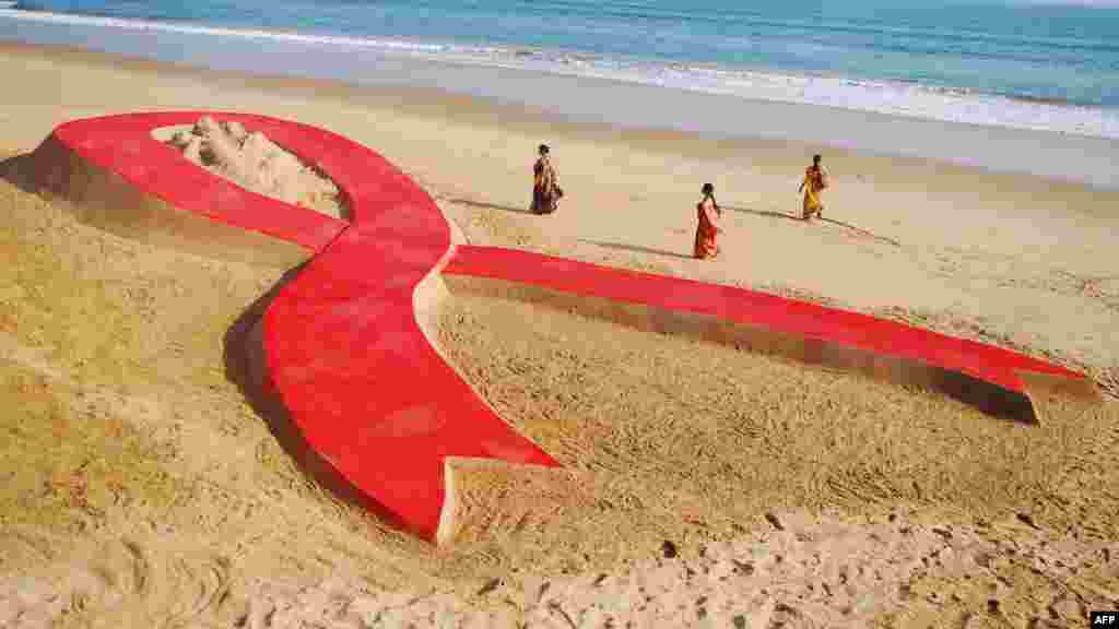 Indian women walk past a 30-meter-long sand sculpture in the shape of a ribbon in Konark on November 30, created as part of an awareness campaign on the eve of World AIDS Day. (AFP)