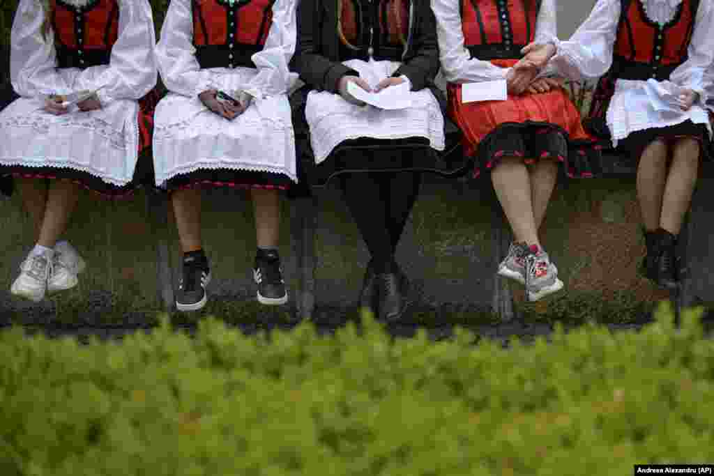 Девушки в традиционной одежде (но не в традиционной обуви) отдыхают во время католического паломничества, которое посетили десятки тысяч людей в Сумулеу-Чук, Румыния
