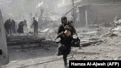 Një grua siriane mban një fëmijë derisa ikën nga sulmet ajrore të qeverisë siriane në enklavën e mbajtur nga rebelët në Ghouta, në periferi të kryeqytetit Damask. 