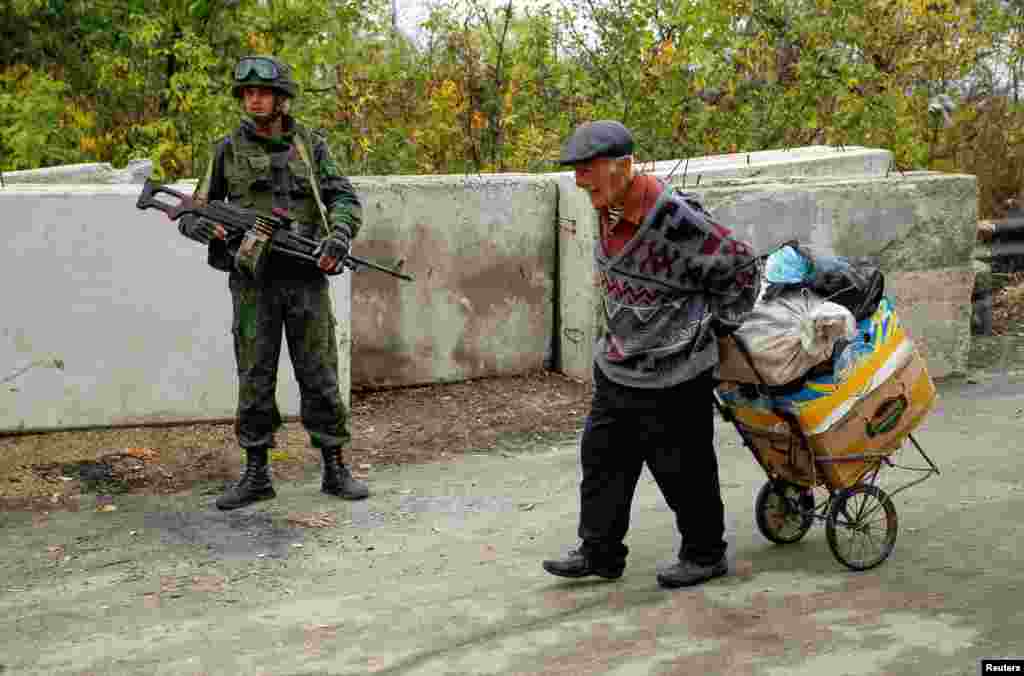 A man carries his belongings past a Russia-backed separatist in the settlement of Stanytsia Luhanska in the Luhansk region of eastern Ukraine. (Reuters/Alexander Ermochenko)