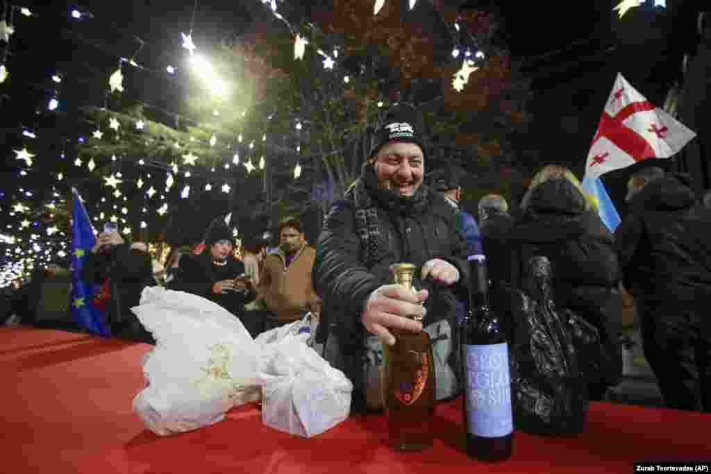 A man in Tbilisi opens a drink as other people gather in a street decorated for the Christmas and New Year festivities.&nbsp;