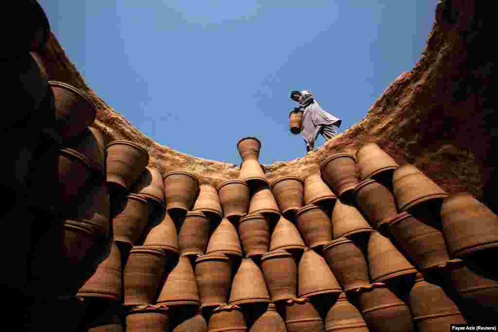 A Pakistani man carries a clay pot to place it with others inside an oven at a makeshift factory in Peshawar. (Reuters/Fayaz Aziz)