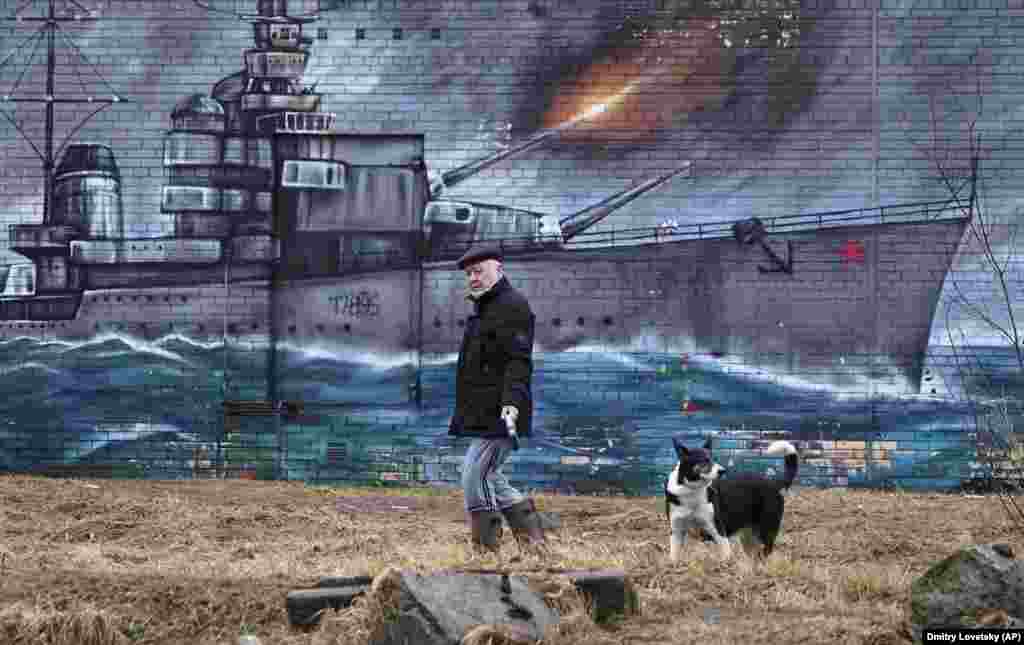 A man and his dog walk past graffiti on a wall in St. Petersburg depicting a World War II era Soviet warship. (AP/Dmitri Lovetsky)