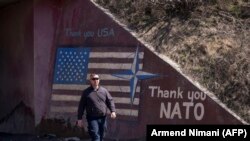 Një person kalon pran një grafiti ku shkruan “Faleminderit SHBA” dhe “Faleminderit NATO”. 