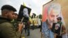 Supporters of the Hashed al-Shaabi paramilitary force and Iraq's Hezbollah brigades pose for a picture next to a poster of Iranian military commander Qassem Soleimani. January 4, 2020