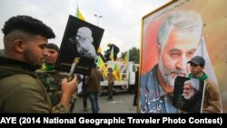 Supporters of the Hashed al-Shaabi paramilitary force and Iraq's Hezbollah brigades pose for a picture next to a poster of Iranian military commander Qassem Soleimani. January 4, 2020