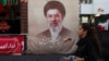 A woman in Tehran walks next to a banner with a picture of Iranian Supreme Leader Mojtaba Khamenei. 