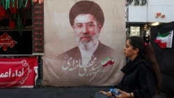 A woman in Tehran walks next to a banner with a picture of Iranian Supreme Leader Mojtaba Khamenei. 