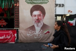 A woman walks next to a banner with a picture of Iran's Supreme Leader Mojtaba Khamenei in Tehran on August 13.