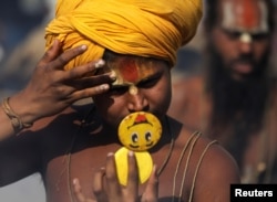 Un hindus se uită într-o oglindă în timp ce se pregătește pentru rugăciunile de dimineață, pe malurile râului Gange