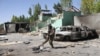 An Afghan soldier stands guard next to damaged army vehicles after a Taliban attack in the southeastren city of Ghazni on August 15.