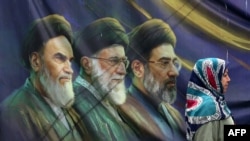 یک زن ایرانی از کنار یک پوستر از تصاویر رهبران فقید و جدید ایران عبور می کند