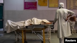 یک مرد در هند نزدیک جسد همسرش که در اثر ابتلا به ویروس کرونا جان باخته ایستاده است.