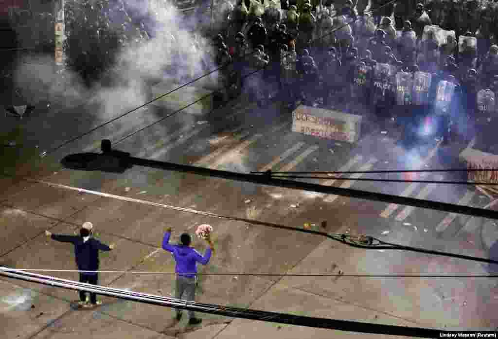 Doi protestatari în fața poliției care folosește gaze lacrimogene împotriva manifestanților, în apropierea Departamentului de Poliție din Seattle, SUA, 8 iunie 2020.