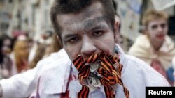 Un protestatar costumat în zombie ține în gură o bucată de ziar și mai multe panglici Sf.Gheorghe la o demonstrație împotriva propagandei ruse, Kiev, 21 iunie 2015.