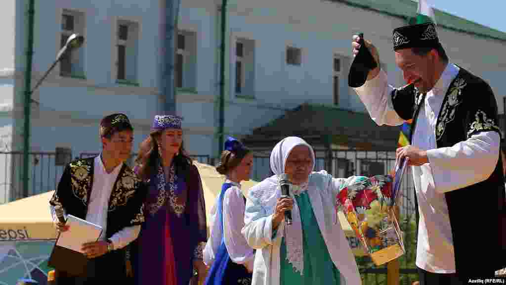 Алып баручы, Камал артисты Фәнис Җиһанша Татар бистәсенең иң өлкән вәкиле Нурания апа алып килгән бүләкләрне күрсәтә