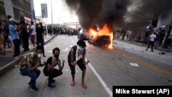 Policijsko vozilo u plamenu dok ljudi poziraju za fotografiju tokom demonstracija protiv policijskog nasilja u Atlanti 29. maja.