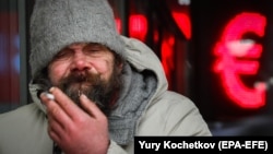 Бездомный курит перед электронной панелью обменного пункта в Москве, 11 февраля 2021 года. Иллюстративное фото
