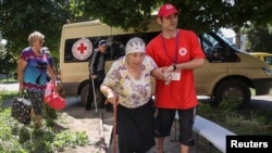 Egy vöröskeresztes önkéntes segít egy idős asszonynak az evakuálásban a Harkivi területen lévő Kupjanszk-Vuzlovij városból az Ukrajna elleni orosz támadás közepette