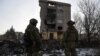 Militari ucraineni stau lângă o clădire rezidențială grav avariată în timpul unei lovituri militare rusești la Bahmut.