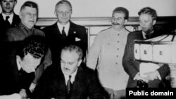 Ministrul de externe sovietic Viaceslav Molotov semenază pactul de neagresiune dintre Uniunea Sovietică şi Germania nazistă. În spatele lui se află Ribbentrop şi Stalin, 23 august 1939.