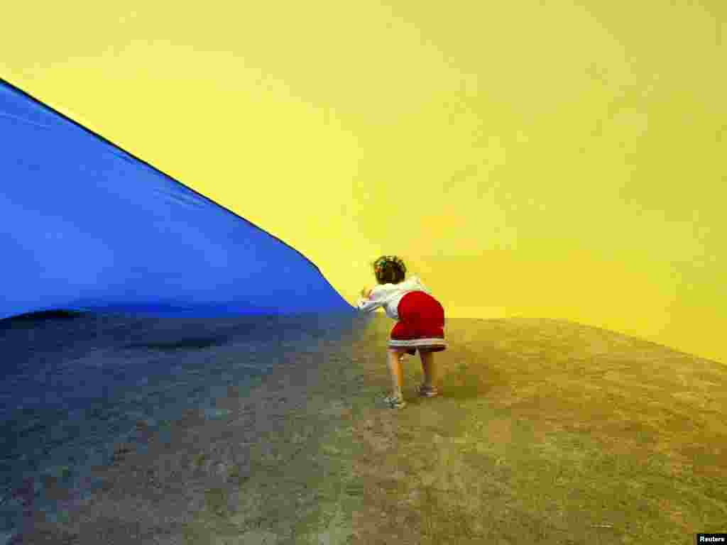 A girl walks under a giant Ukrainian national flag, held by people celebrating the Day of the State Flag in Kyiv on August 23.Photo by Konstantin Chernichkin for Reuters