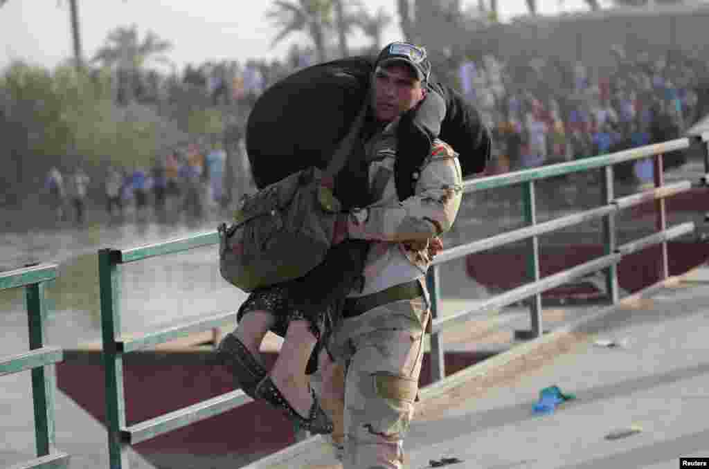 An Iraqi soldier helps a displaced woman cross a bridge at the outskirts of Baghdad. (Reuters/Stringer)