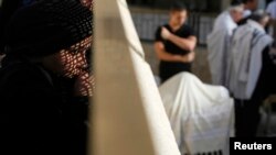 O femeie privind din spatele unui perete metalic la bărbații care se roagă la Zidul Plîngerii la Ierusalim.
