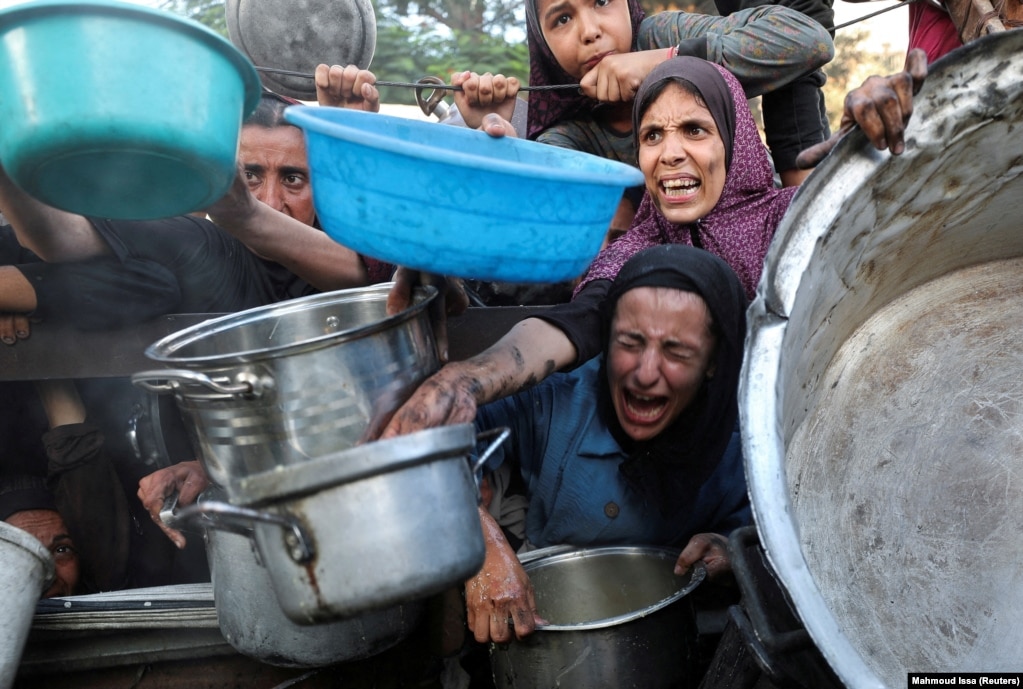 Palestinezë të uritur duke zgjatur enët për të marrë ushqim nga një kuzhinë popullore, më 14 korrik.