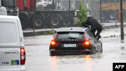 Një burrë del nga dritarja e veturës që po lëvizte në një rrugë të vërshuar në Arlöv, të Suedisë, më 7 gusht 2023.