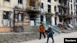 Місцеві жителі проходять повз багатоповерхівку, зруйновану під час штурмів військ Росії Маруполя, 16 березня 2023 року