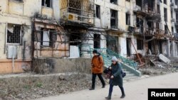 Локални жители шетаат покрај разурнати згради во Мариупол