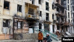 Helyiek sétálnak egy lerombolt épület előtt Mariupolban 2023. március 16-án