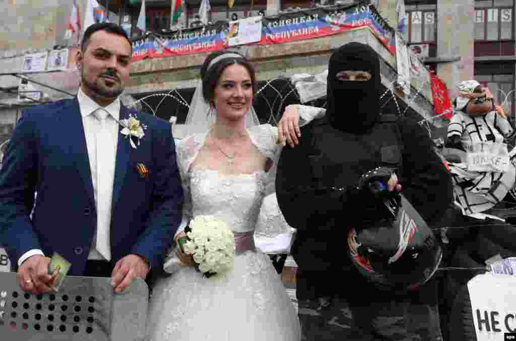 A couple on their wedding day poses with a masked and armed man at the barricades in the center of downtown Donetsk, Ukraine, 02 May 2014.