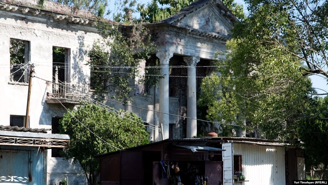 Georgia -- People rest near small shops in-front of ruined hospital building in Bargebi village in Gali region of Abkhazia, 25Aug2011