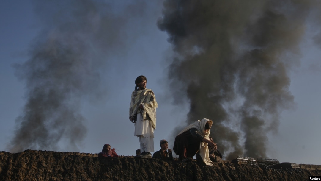Smoke rises past residents standing on the wall of a truck terminal where NATO fuel tankers were set ablaze in Quetta on December 9.
