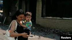 A woman carries a baby as she passes destroyed houses following what locals say was overnight shelling by Ukrainian forces in the eastern town of Slovyansk on June 9.