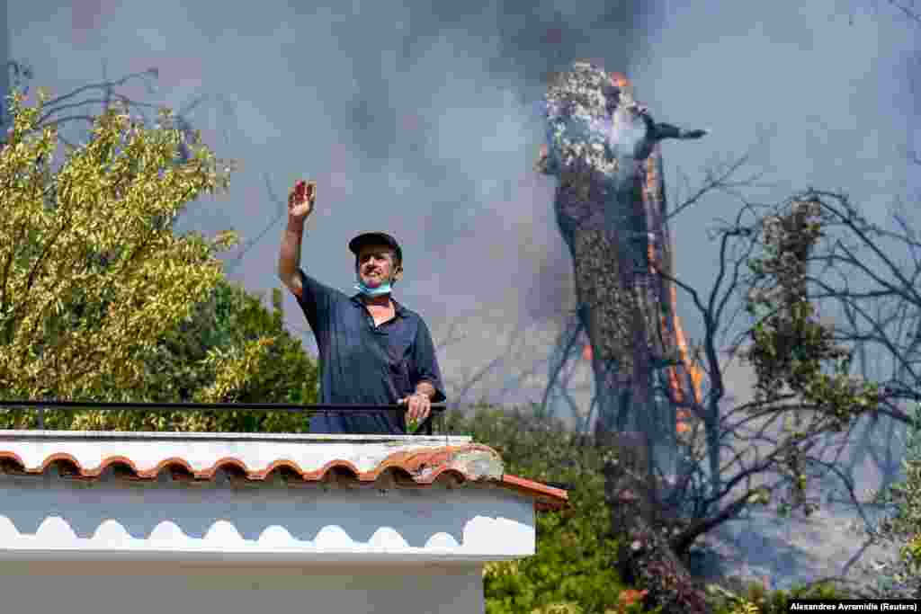 Një vendës duke qëndruar në ballkonin e tij, teksa një zjarr i egër përhapej afër fshatit të Vasilikës, në ishullin e Evias, në Greqi. (8 gusht)