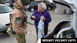 A Ukrainian border guard wearing a protective face mask searches a car and checks the passport of a woman leaving Ukraine and heading into territory controlled by Russia-backed separatists at the checkpoint near Novotroitske in the Donetsk region on March 16.