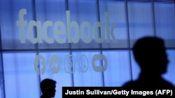 Силуэты на фоне логотипа американской интернет-компании Facebook.