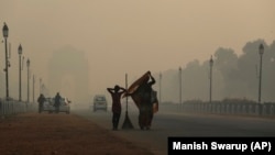 Një punëtor komune me vajzën e tij duke ecur nëpër shtresa smogu në Delhi të Indisë.