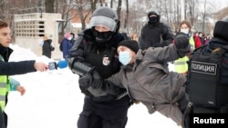 Un bărbat care poartă o vestă de presă întinde un microfon în timp ce poliția reține un protestatar în timpul unui miting împotriva arestării lui Alexei Navalnîi