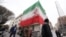 TOPSHOT - A huge Iranian flag adorns a building as Iranians walk past damaged structures following an earlier military strike in the Iranian capital, Tehran, on March 15, 2026.